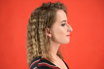 Close-up portrait of a smiling female model with excellent make-up in the studio on a red background. The concept of applying cosmetics, anti-aging makeup.