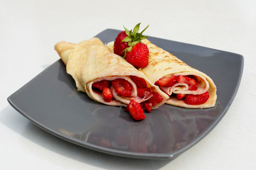 Rolled crepes or balkan pancakes stuffed fresh chopped strawberries. Gourmet sweet dish