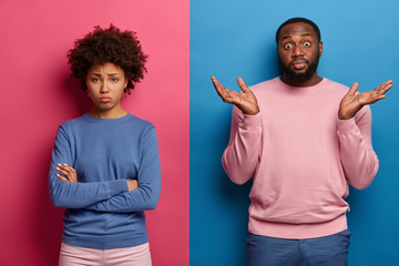 Hesitant black man spreads palms with hesitation, doesnt know how to calm girlfriend who stands...