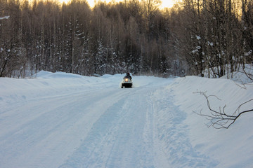 two people ride a snowmobile in the cold on a cleared snowy road in the forest . active rest in the winter.