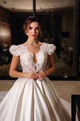 beautiful bride with dark hair in elegant wedding dress posing in luxurious interior