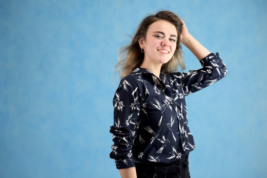 Concept woman in a dark blouse smiling talking. Portrait of a model girl with excellent makeup with curly hair and good teeth in the studio on a blue background.