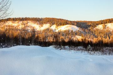 snow-covered hills, evergreen trees on the slopes, in the sunset. Lots of snow and frost trees. 