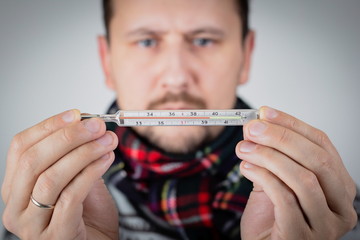 a young european man withba mustache holds a mercury thermometer in his hands and frowns because it shows a high temperature