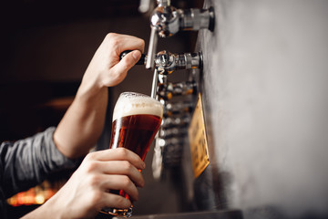 Bartender pours beer from tap into glass, dark background. Alcohol craft drink concept