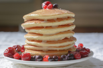 Homemade pancakes with berries and  condensed milk on white plate isolated