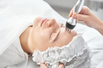 Obraz na płótnie Canvas Professional beautician in office conducts session of thermal or radio frequency hardware RF lifting. Tightening and rejuvenation of face skin woman patient close up