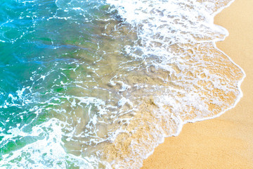 Ocean wave on tropical beach with golden sand and ripple of water splash from emerald blue-green sea water during summer vacation.