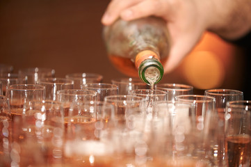 Hand hält eine Flasche mit Spirituosen und füllt braunen Alkohol in kleine Gläser