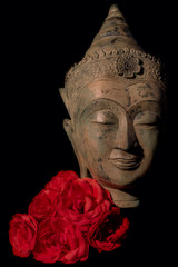 Fototapeta na wymiar Traditional Buddha head statue with red roses. Buddhism and love.