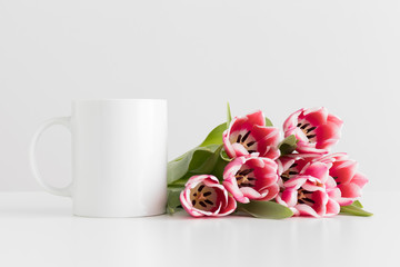 Mug mockup with bouquet of pink tulips on a white table.