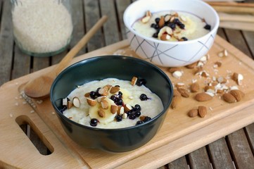 Creamy rice porridge with almond and fruit in bowl on wooden background