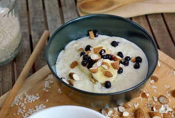 Creamy rice porridge with almond and fruit in bowl on wooden background