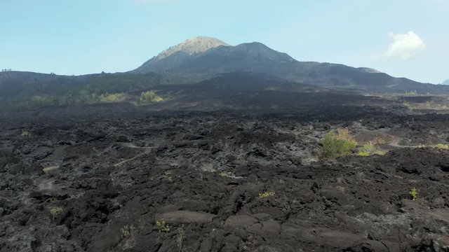 Aerial drone view flying over cold, black volcanic lava flows from an active volcano (Mount Batur, Bali, Indonesia)
