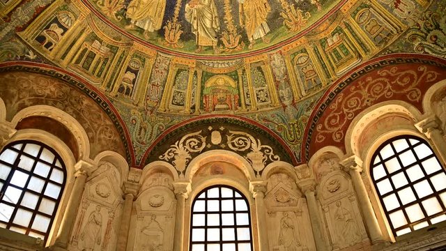 Ravenna, Italy, December 2019. Inside the Neonian Baptistery (or the Orthodox), tilt movement from the bottom towards the vault decorated with incredible mosaics. Warm yellowish light illuminates them