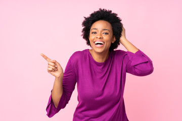 African american woman over isolated pink background surprised and pointing finger to the side