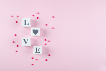 Love message written in white wooden blocks on pink background. Pink candy hearts. Flat lay, top view, copy space