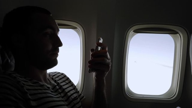 Man looking through pictures on his phone sitting in a plane.