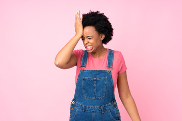 African american woman with overalls over isolated pink background having doubts with confuse face expression