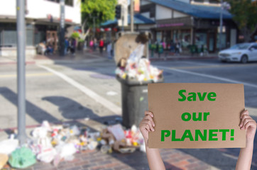 Boy's hands holding banner call to save our planet in front of a big pile of human trash during summer time