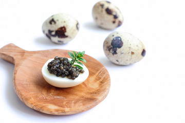 Delicious black sturgeon caviar on a quail egg with rosemary on the wooden plate and fresh quail...