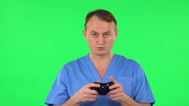 Medical man playing a video game using wireless controller and rejoicing in victory. Green screen