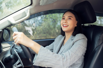 Fototapeta na wymiar Safety driving concept, Smiling happy young Chinese Thai Asian businesswoman driving a car in town, Confident and beautiful girl. Rear view woman in business suit wear looking over her shoulder