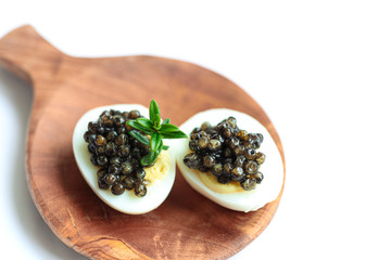Gourmet dish, delicious black sturgeon caviar on a quail eggs on the wooden plate isolated on the...