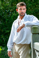 Portrait of handsome gentleman dressed in vintage costume standing on bridge of stately home with...