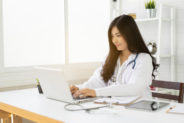 Obraz na płótnie Canvas Asian female doctor sitting at hospital office desk giving all patient convenience online service advice and smiling write a prescription on laptop to order medical,health care and preventing disease