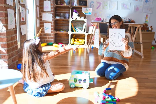 Beautiful pshychologist and toddler doing therapy with emotions emoji around lots of toys at kindergarten