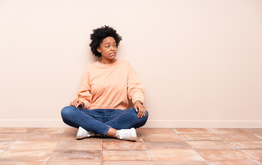 African american woman sitting on the floor with confuse face expression