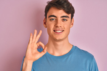 Teenager boy wearing casual t-shirt standing over blue isolated background doing ok sign with fingers, excellent symbol