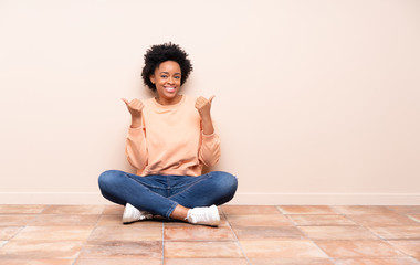 African american woman sitting on the floor with thumbs up gesture and smiling