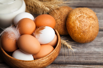 Fresh white and brown chicken eggs in a wooden bowl, milk, bread, and wheat ears. Raw eggs on wooden background