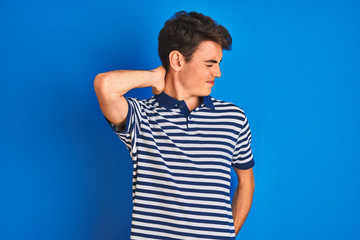 Teenager boy wearing casual t-shirt standing over blue isolated background Suffering of neck ache injury, touching neck with hand, muscular pain