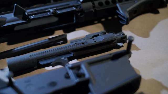 slow pan across disassembled ar-15 rifle in a pistol configuration. The shot slides across the charging handle, the bolt carrier group and the lower assembly.