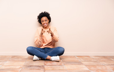 African american woman sitting on the floor pointing to the front and smiling