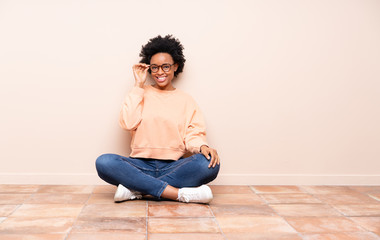 African american woman sitting on the floor with glasses and happy