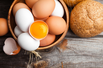 Raw broken egg with yolk in a wooden bowl. Fresh white and brown chicken eggs on wooden background