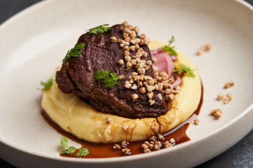 Stewed veal cheeks with mashed potatoes on a white plate, close-up.