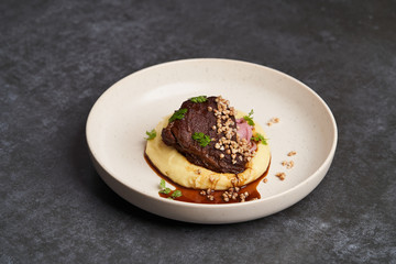 Stewed veal cheeks with mashed potatoes on a white plate, close-up.