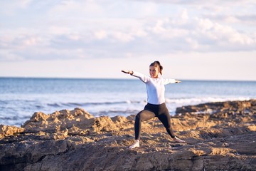 Young beautiful sportwoman practicing yoga. Coach teaching warrior pose at the beach