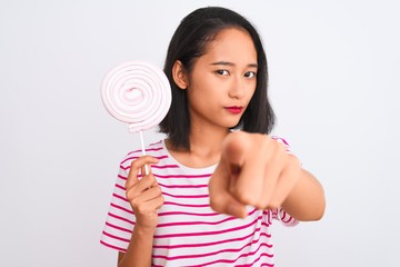 Young beautiful chinese woman eating lollipop standing over isolated white background pointing with finger to the camera and to you, hand sign, positive and confident gesture from the front