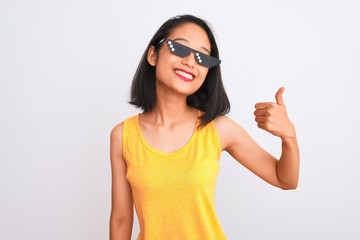 Young beautiful chinese woman wearing thug life sunglasses over isolated white background doing happy thumbs up gesture with hand. Approving expression looking at the camera with showing success.