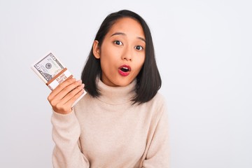 Young beautiful chinese woman holding dollars standing over isolated white background scared in shock with a surprise face, afraid and excited with fear expression