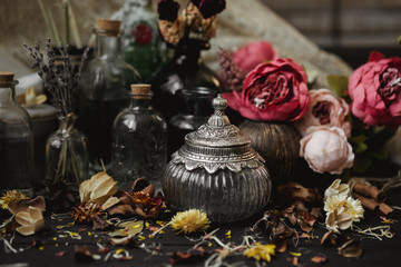 vintage jars, bottles, containers, flowers in smoke and dry leaves on a wooden table with warm light