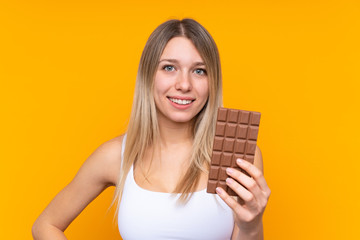 Young blonde woman over isolated blue background taking a chocolate tablet and happy