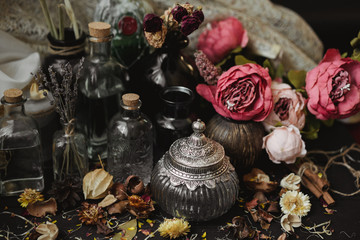 vintage jars, bottles, containers, flowers in smoke and dry leaves on a wooden table with warm light