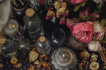 vintage jars, bottles, containers, flowers in smoke and dry leaves on a wooden table with warm light